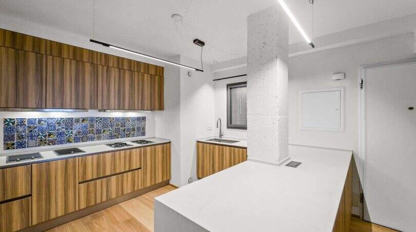 Moderne Küche der Luxuswohnung in Palma mit Holzfronten, weißer Insel und bunten Azulejo-Fliesen.