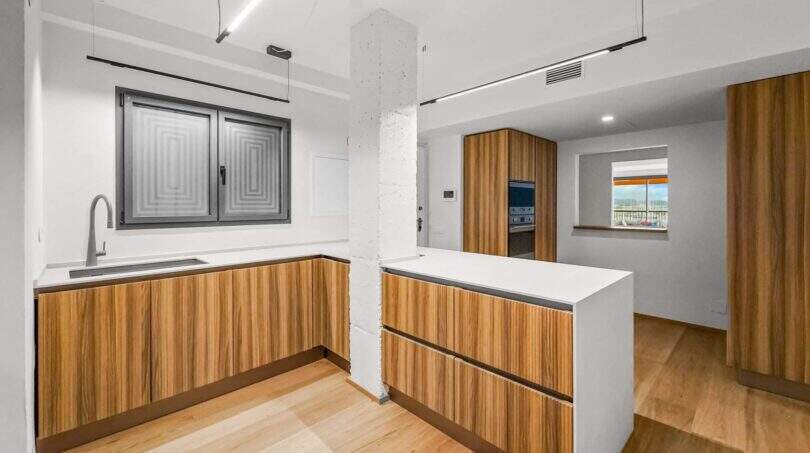 Moderne Küche der Luxuswohnung in Palma mit Holzfronten, weißer Kochinsel und elegantem Lichtdesign.