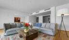 Helles Wohnzimmer der Luxuswohnung am Paseo Marítimo mit grauen Sofas, Glastisch und buntem Teppich.