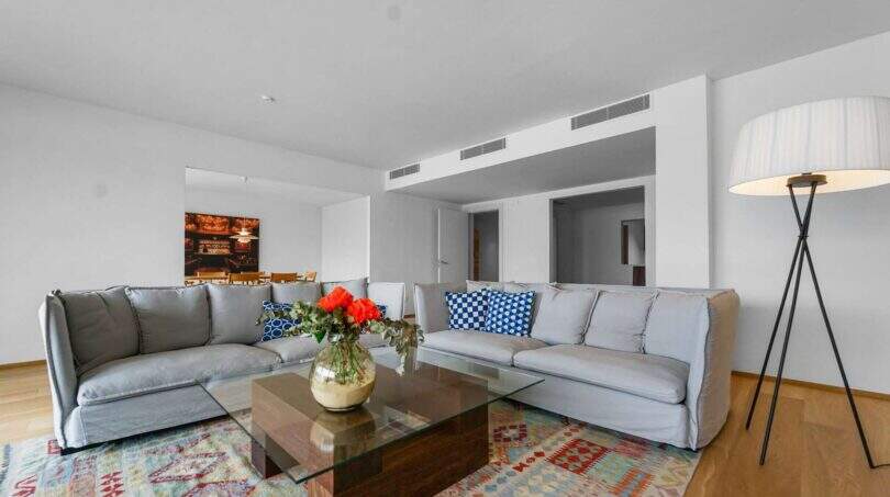 Helles Wohnzimmer der Luxuswohnung am Paseo Marítimo mit grauen Sofas, Glastisch und buntem Teppich.