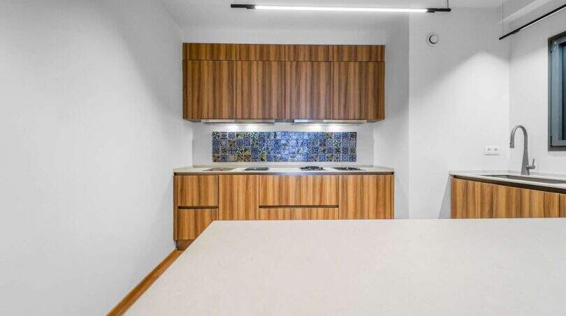 Moderne Küche der Luxuswohnung in Palma mit Holzfronten und dekorativen Azulejos-Fliesen als Wandverkleidung.