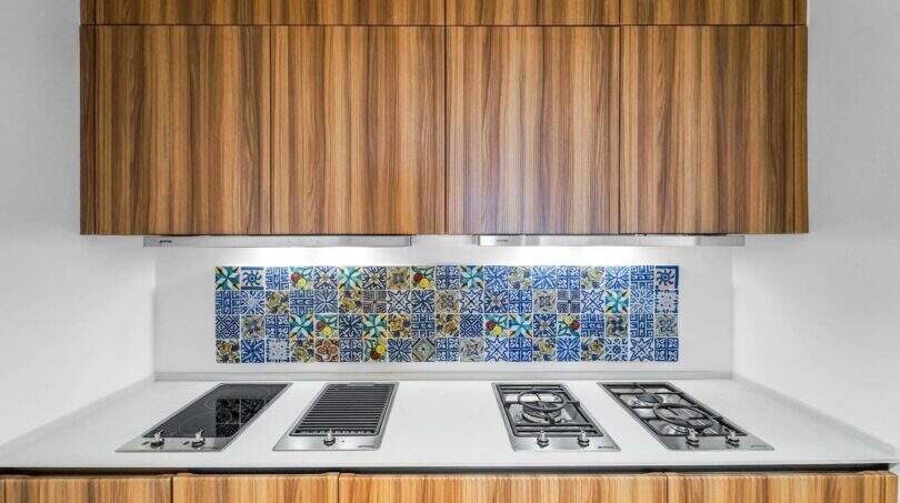 Moderne Küche der Luxuswohnung in Palma mit Holzfronten, weißer Arbeitsfläche und bunten Mittelmeer-Fliesen.