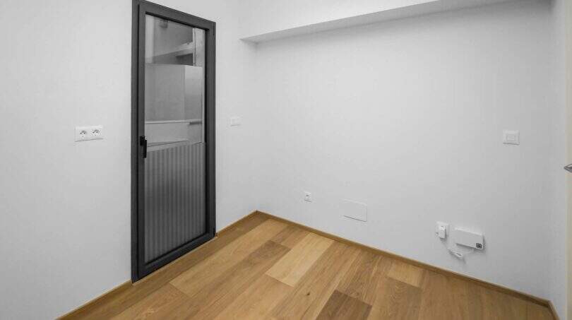 Leeres Zimmer der Luxuswohnung in Palma mit Holzboden, weißen Wänden und moderner Glastür.