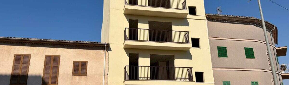 Mehrstöckiges Wohngebäude im Rohbau mit Balkonen in Manacor, flankiert von Nachbargebäuden, sonnige Außenansicht.