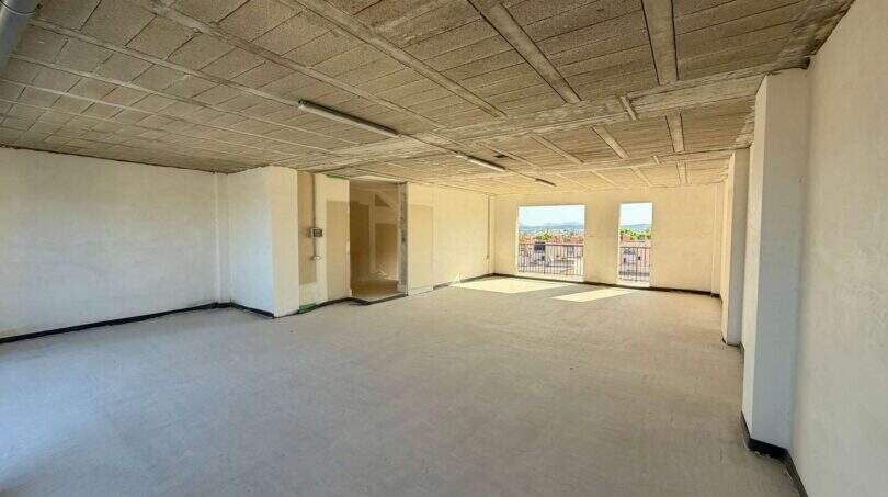 Leerer Rohbau-Raum mit Betondecke, hellen Wänden und Fenstern mit Ausblick auf Manacor