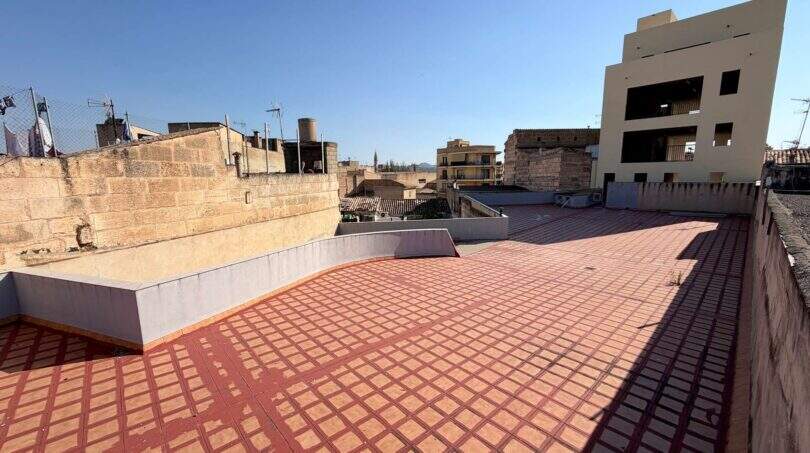 Großzügige Dachterrasse mit roten Fliesen und Blick über die Dächer von Manacor bei blauem Himmel.