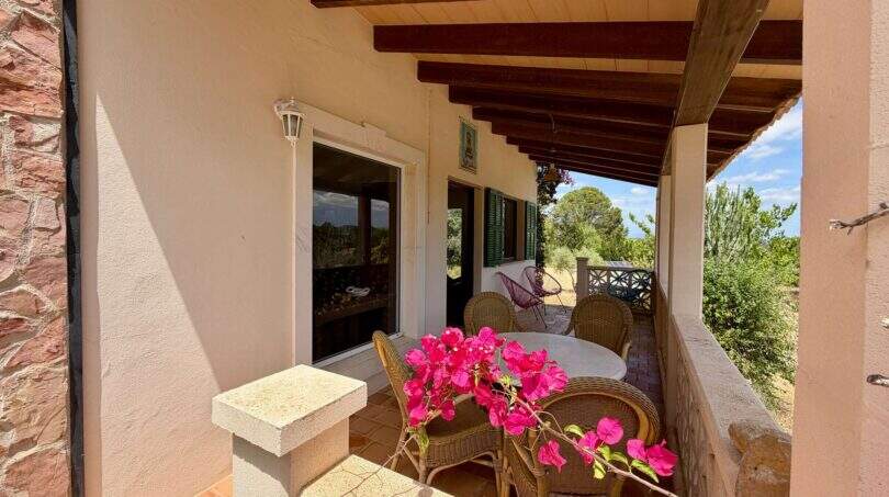 Überdachte Terrasse der Finca bei Sant Joan mit Rattanmöbeln, Holzbalkendecke und blühender Bougainvillea
