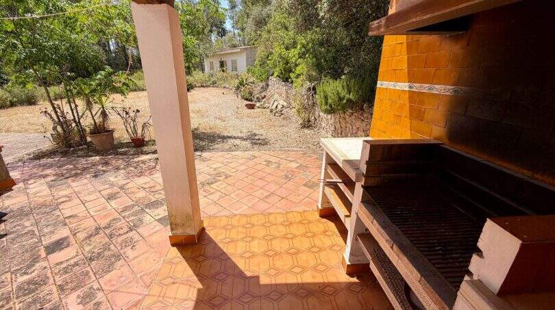 Überdachte Terrasse mit Grillstation und Terrakottafliesen, Blick auf den naturnahen Garten der Finca bei Vilafranca