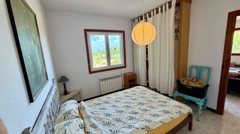 Helles Schlafzimmer der Finca bei Vilafranca mit Doppelbett, Pendelleuchte und Fenster mit Grünblick.