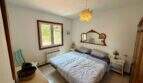 Helles Schlafzimmer der Finca mit Doppelbett, Vintage-Spiegel, Kronleuchter und Fenster mit Gartenblick.