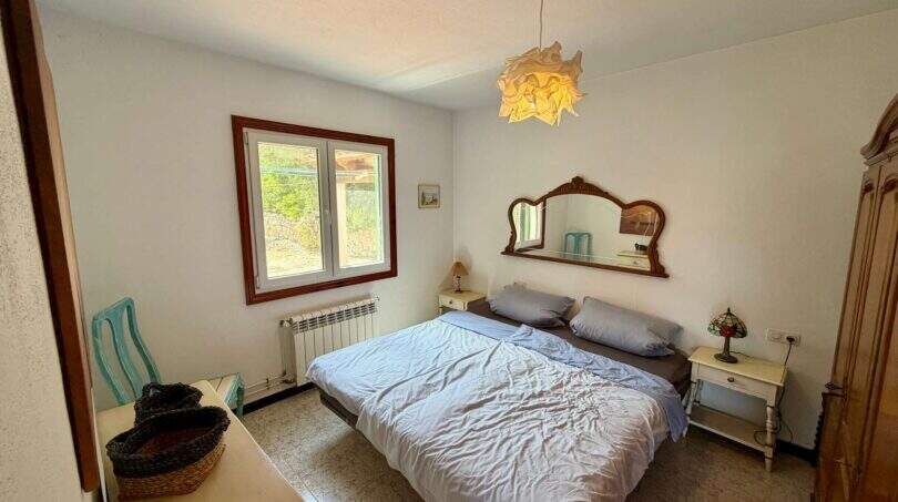 Helles Schlafzimmer der Finca mit Doppelbett, Vintage-Spiegel, Kronleuchter und Fenster mit Gartenblick.