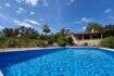 Großer blauer Pool vor rustikaler Finca mit Terrasse, Palme und Pinienwald unter blauem Himmel in Sant Joan