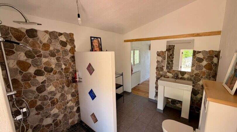 Badezimmer der Finca mit Natursteinwand, bodenebener Dusche, Waschbecken und WC