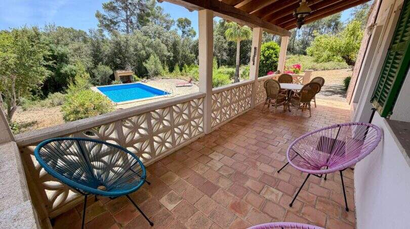 Überdachte Terrasse der Finca mit bunten Acapulco-Stühlen, Blick auf Pool und grüne Natur in Sant Joan