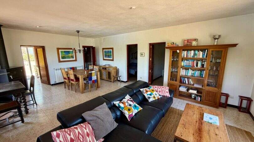 Geräumiges Wohnzimmer der Finca mit schwarzem Ledersofa, Holzcouchtisch, Bücherregal und offenem Essbereich