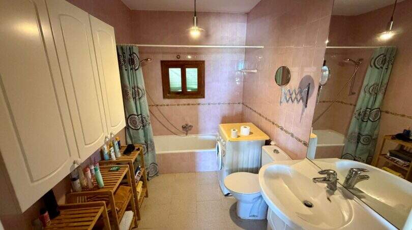 Geräumiges Badezimmer der Finca bei Vilafranca de Bonany mit Badewanne, Dusche, Waschbecken und rosa Wandfliesen.
