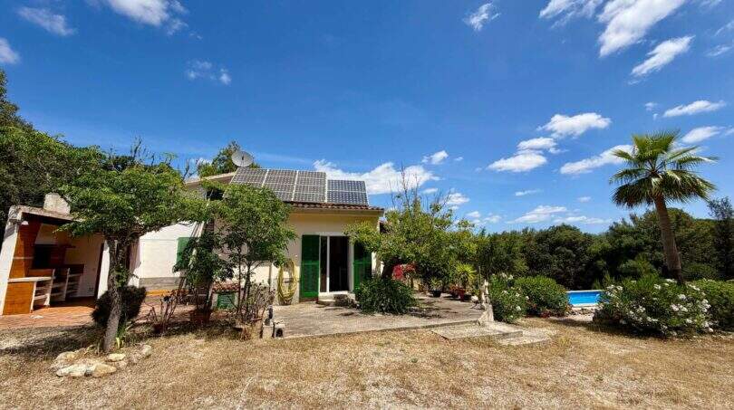 Außenansicht der Finca bei Sant Joan mit Solaranlage, Pool, Palme und üppigem Grün unter blauem Himmel.