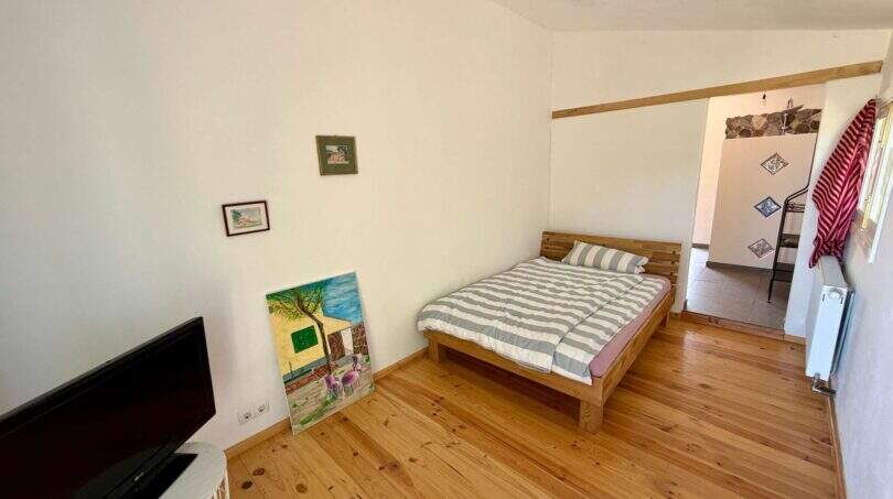 Schlafzimmer der Finca mit Holzboden, Doppelbett, TV und Durchgang zum Bad