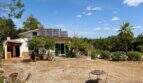 Außenansicht der Finca bei Sant Joan mit Solarpanelen, Satellitenantenne, grünen Fensterläden und Palme im Garten
