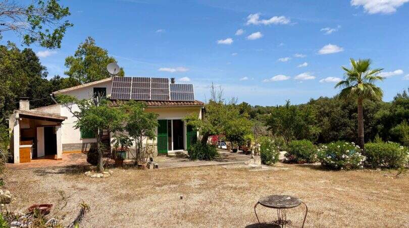 Außenansicht der Finca bei Sant Joan mit Solarpanelen, Satellitenantenne, grünen Fensterläden und Palme im Garten
