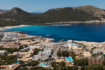 Luftaufnahme von Cala Ratjada mit türkisblauem Meer, Sandstrand und Hotelanlage, umgeben von grünen Hügeln.