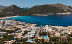 Luftaufnahme von Cala Ratjada mit türkisblauem Meer, Sandstrand und Hotelanlage, umgeben von grünen Hügeln.