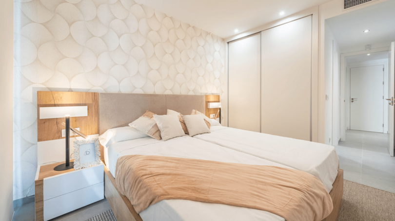 Helles Schlafzimmer mit Doppelbett, Holzelemente und gemusterter Tapete in Wohnung Cala Ratjada