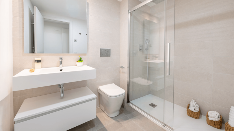 Modernes Badezimmer der EG-Wohnung in Cala Ratjada mit Glasdusche, Waschtisch und hellen Fliesen.