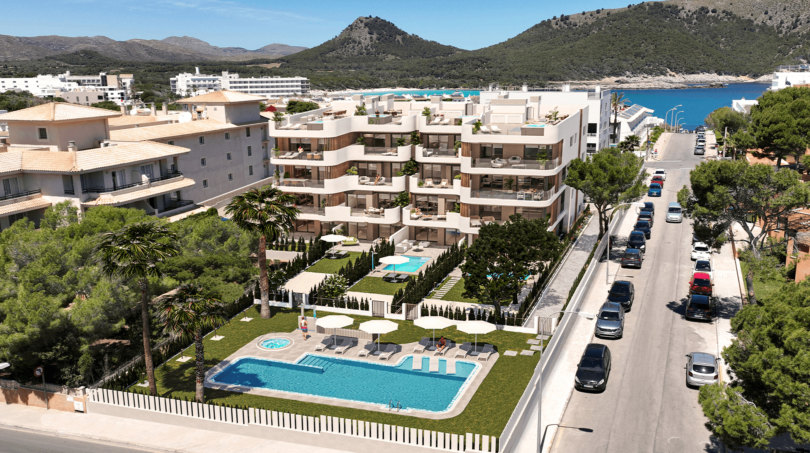 Luftansicht moderner Wohnanlage in Cala Ratjada mit Pool, Gartenanlage und Meerblick vor Bergkulisse.