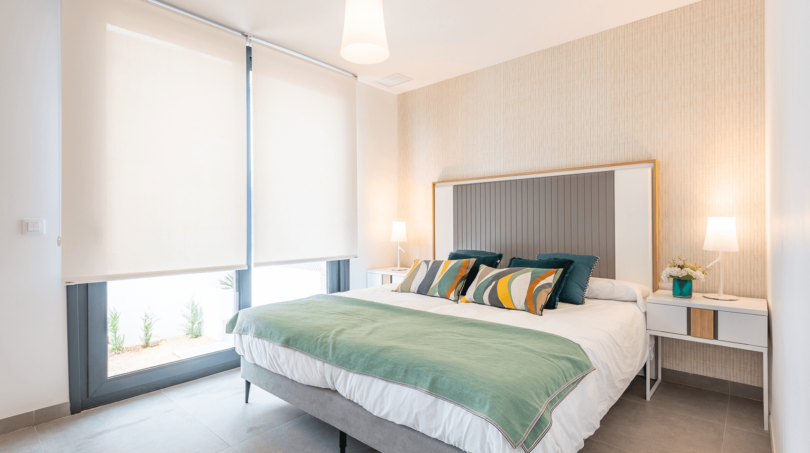 Helles Schlafzimmer der DHH in Cala Ratjada mit Doppelbett, grüner Tagesdecke und großem Fenster mit Gartenblick.