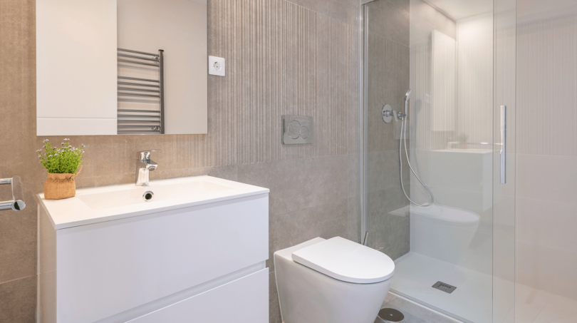 Modernes Badezimmer der DHH in Cala Ratjada mit Glasdusche, weißem Waschtisch und grauer Wandverkleidung.