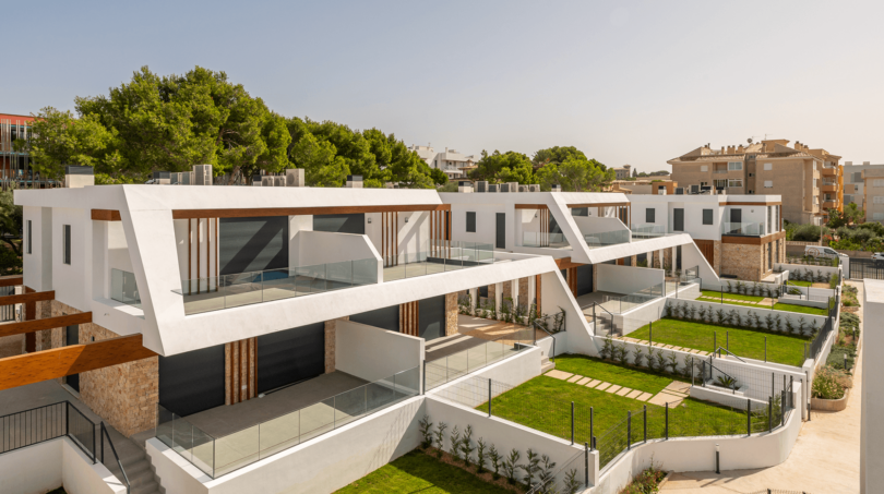 Modern semi-detached houses in Cala Ratjada with glass railings, wood accents and well-maintained green spaces.