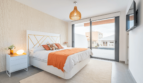 Helles Schlafzimmer der DHH in Cala Ratjada mit Doppelbett, orangenen Akzenten und Balkonzugang