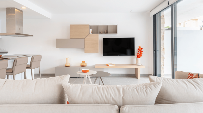 Helles Wohnzimmer der DHH in Cala Ratjada mit modernem TV-Bereich, Holzelementen und Zugang zur Terrasse.