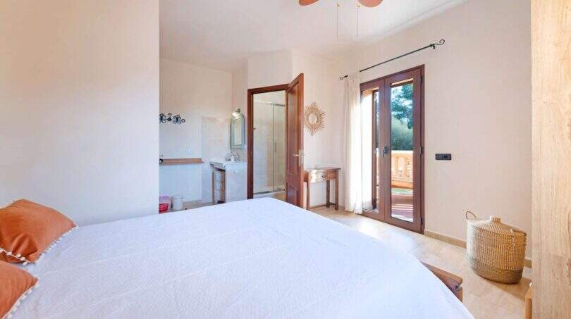 Luminoso dormitorio de la finca Portocolom con cama doble, baño en suite, ventilador de techo y acceso a terraza.