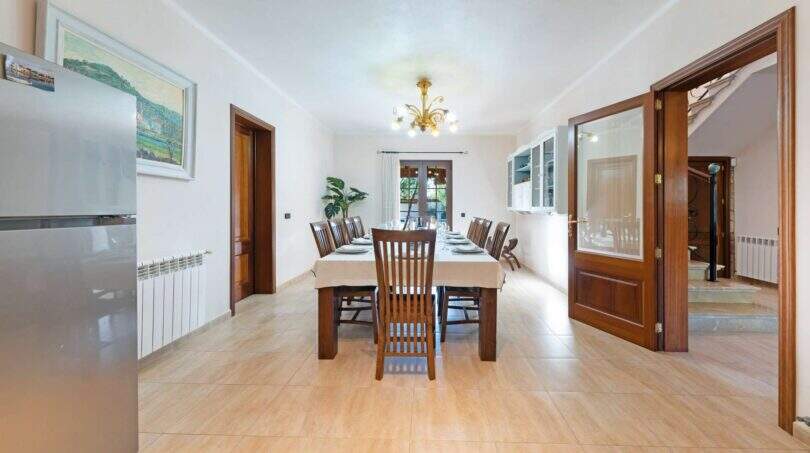 Amplio comedor de la Finca en Portocolom con mesa de madera larga, lámpara de araña y suelo de azulejos luminoso.
