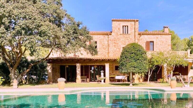 Finca rústica en Portocolom con gran piscina, muros de piedra natural y jardín exuberante bajo cielo azul.