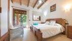 Luminoso dormitorio de la Finca en Portocolom con techo de vigas de madera, cama doble y acceso a terraza al jardín.