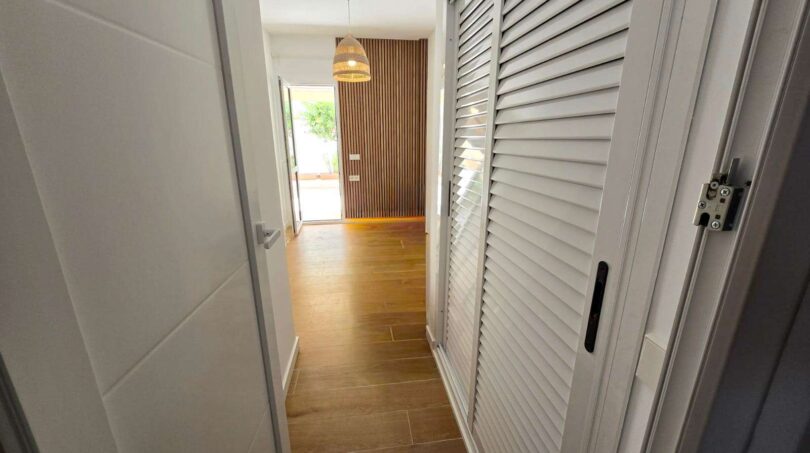 Heller Flur mit weißen Jalousietüren, Holzboden und Holzlamellenwand im Hafenapartment Portocolom