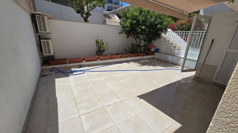 Heller Innenhof mit Fliesenboden, Gartenschlauch, Topfpflanzen, Klimaanlage und überdachtem Zugang in Portocolom.