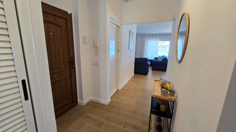 Heller Eingangsflur mit Holzboden, Rundspiegel und Blick ins Wohnzimmer des Hafenapartments in Portocolom