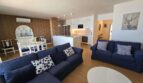 Helles Wohnzimmer mit blauen Sofas, offener Küche und Holzwandverkleidung im Hafenapartment Portocolom