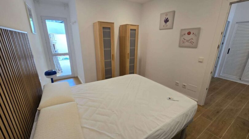 Helles Schlafzimmer mit Doppelbett, Holzschränken und Wandkunst im Hafenapartment Portocolom