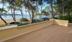 Sonnige Terrasse mit Holzfliesenoptik, Meerblick auf Hafenbucht von Portocolom, Pinien und Sandstrand direkt davor.