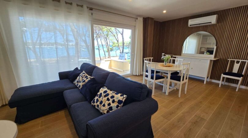 Helles Wohnzimmer mit blauem Sofa, Esstisch und Meerblick durch große Terrassentür in Portocolom