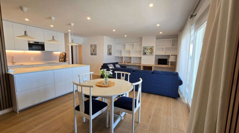 Offener Wohn-Essbereich mit moderner Küche, blauem Sofa und hellem Holzboden im Hafenapartment Portocolom