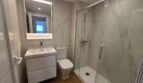 Modernes Badezimmer mit Marmorfliesen, Glasdusche, WC und beleuchtetem Spiegel im Hafenapartment Portocolom