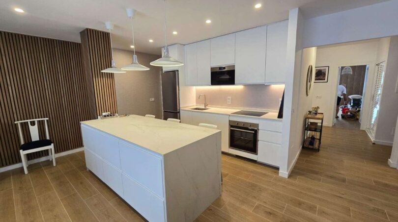 Moderne weiße Küche mit Kücheninsel, Marmor-Arbeitsplatte und Holzboden im Hafenapartment Portocolom