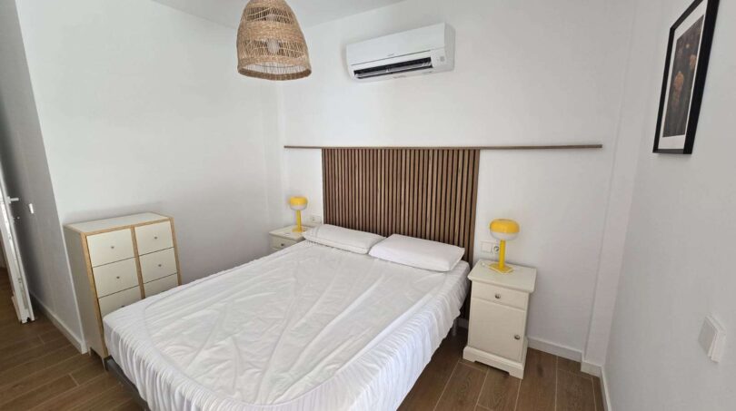 Helles Schlafzimmer mit Doppelbett, Holzkopfteil, gelben Nachttischlampen und Klimaanlage im Hafenapartment Portocolom