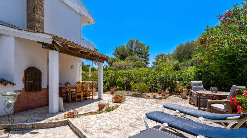 Sonnige Terrasse mit Liegestühlen, überdachtem Essbereich und üppigem Garten in Cala Murada